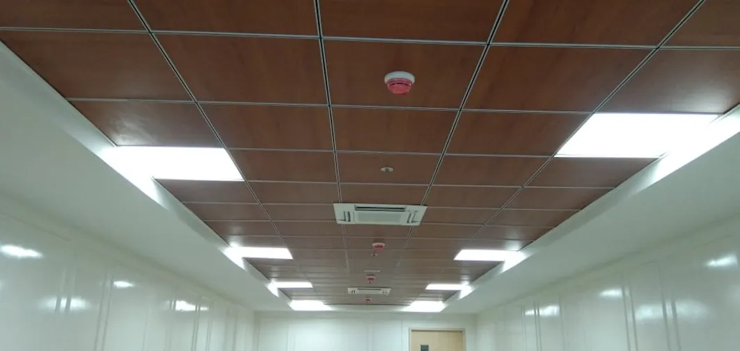 Wood-Finish Grid False Ceiling with Integrated Services – Corridor with Architectural False Ceiling & Lighting at Deskanddecor